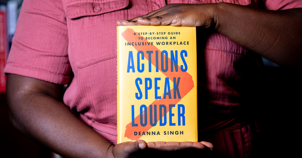 A person holding a copy of Actions Speak Louder by Deanna Singh. 